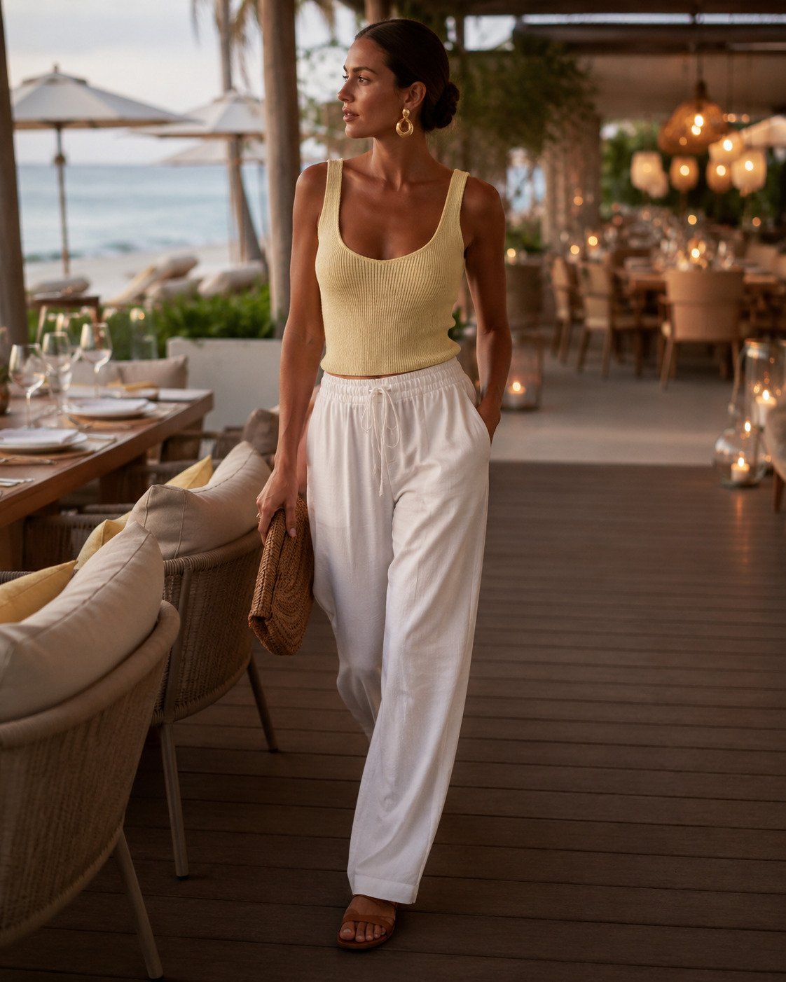 Woman in a butter-yellow knit tank and white drawstring trousers moving from beach club lunch into sunset dinner