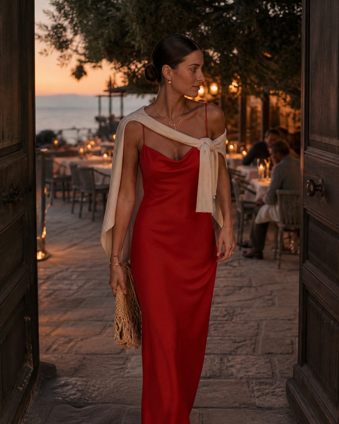 Woman in a tomato-red slip dress heading into a candlelit garden restaurant after the beach